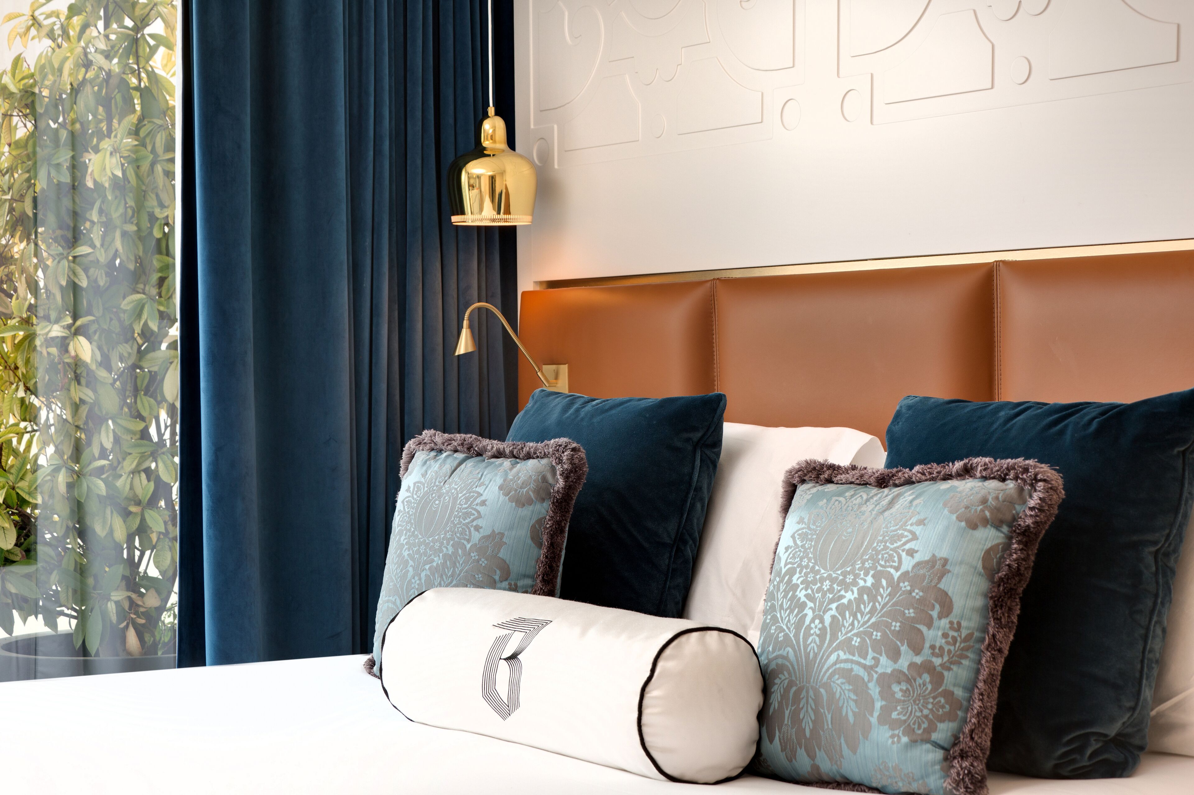 A hotel room with a bed, blue curtains, a wall with a decorative pattern, and a hanging lamp.
