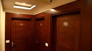 A set of wooden doors with a number plate, a light fixture above, and a wall switch. - Hotel Geetasaar (New Delhi)