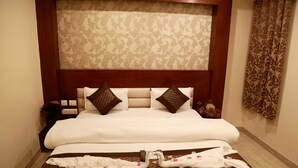 A neatly made bed with a headboard, a remote control, and a pair of slippers on the bed. - Hotel Geetasaar (New Delhi)