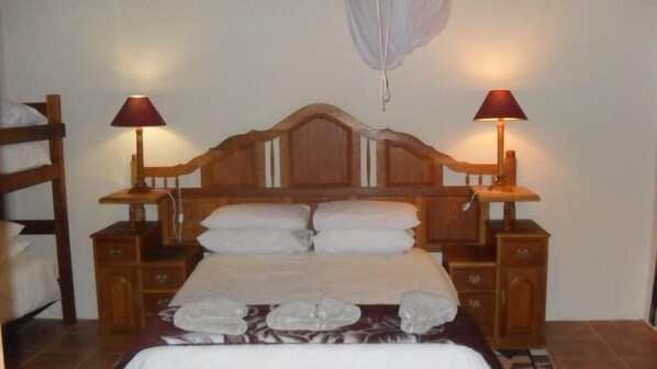 A wooden four-poster bed with white linens, two bedside tables with lamps, and a hanging light fixture.