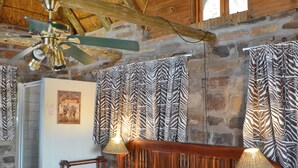Een houten slaapkamer met een bed, nachtkastjes, een plafondventilator en gordijnen met een zebraprint.