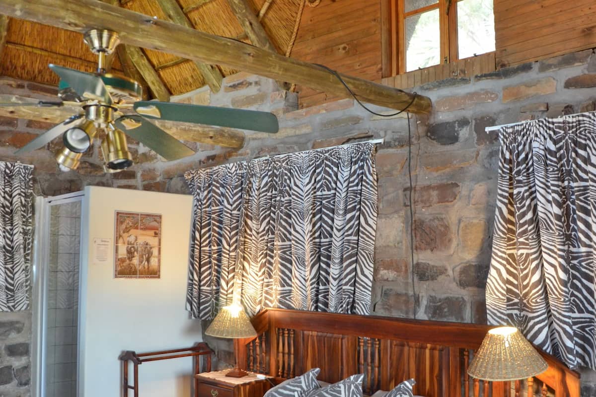 A wooden bedroom with a bed, nightstands, a ceiling fan, and zebra-patterned curtains.
