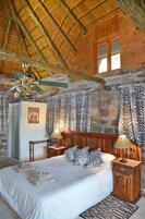 Un dormitorio de madera con cama, mesitas de noche, ventilador de techo y cortinas con estampado de cebra.