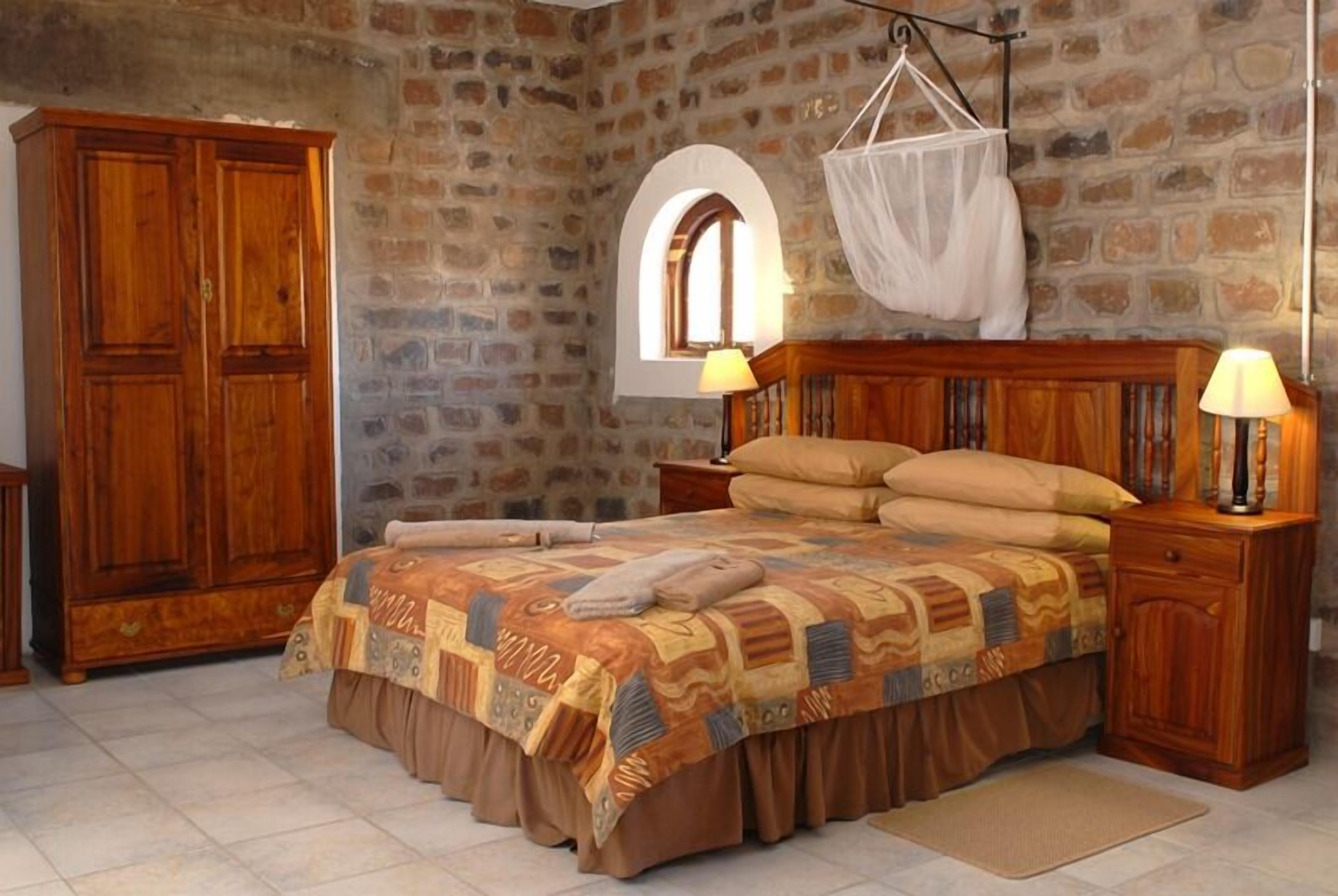Une chambre avec un mur en pierre, un lit en bois, une armoire et une moustiquaire suspendue.