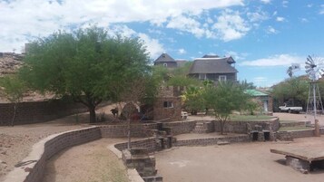 Un patio con muro de piedra, un molino de viento y un edificio con tejado de paja.
