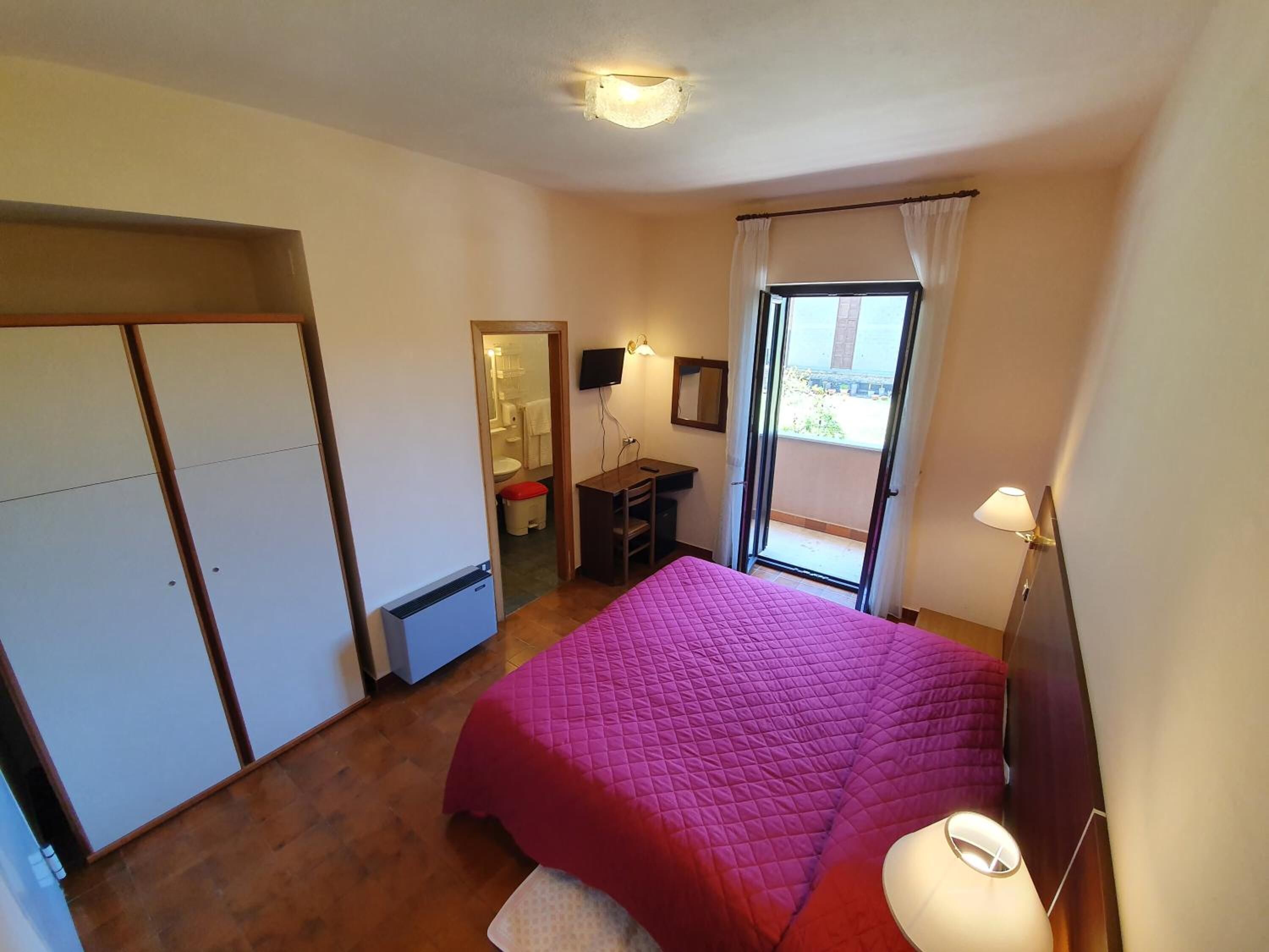 Ein Schlafzimmer mit Bett, Schreibtisch, Stuhl, Kleiderschrank, Badezimmer und einem Balkon mit Aussicht.