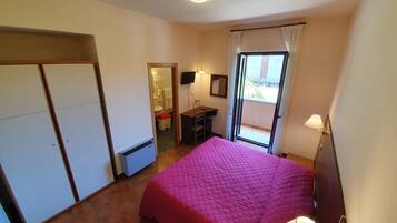 Ein Schlafzimmer mit Bett, Schreibtisch, Stuhl, Kleiderschrank, Badezimmer und einem Balkon mit Aussicht.