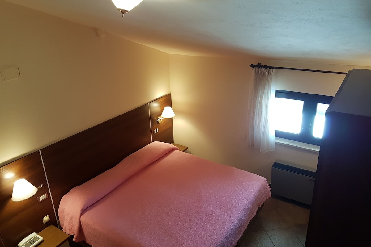 Une chambre d’hôtel avec un lit, des lampes de chevet, une fenêtre avec des rideaux et un luminaire au plafond.