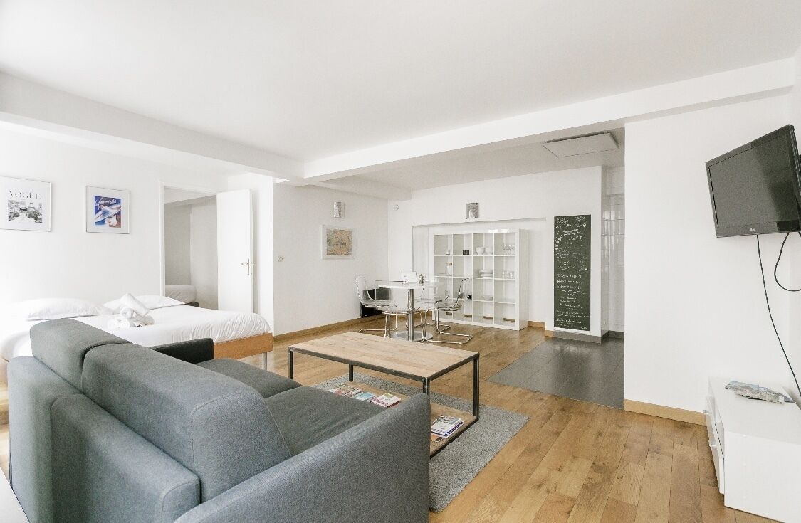 Una sala de estar moderna y luminosa con un sofá gris, una mesa de centro de madera y un televisor blanco en la pared.