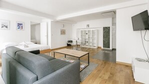 A modern, well-lit living room with a grey sofa, a wooden coffee table, and a white TV on the wall.