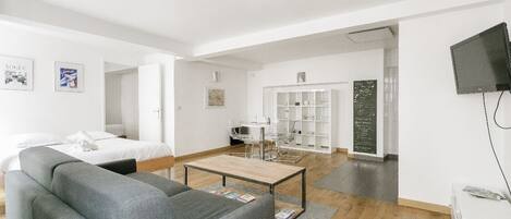 Una sala de estar moderna y luminosa con un sofá gris, una mesa de centro de madera y un televisor blanco en la pared.