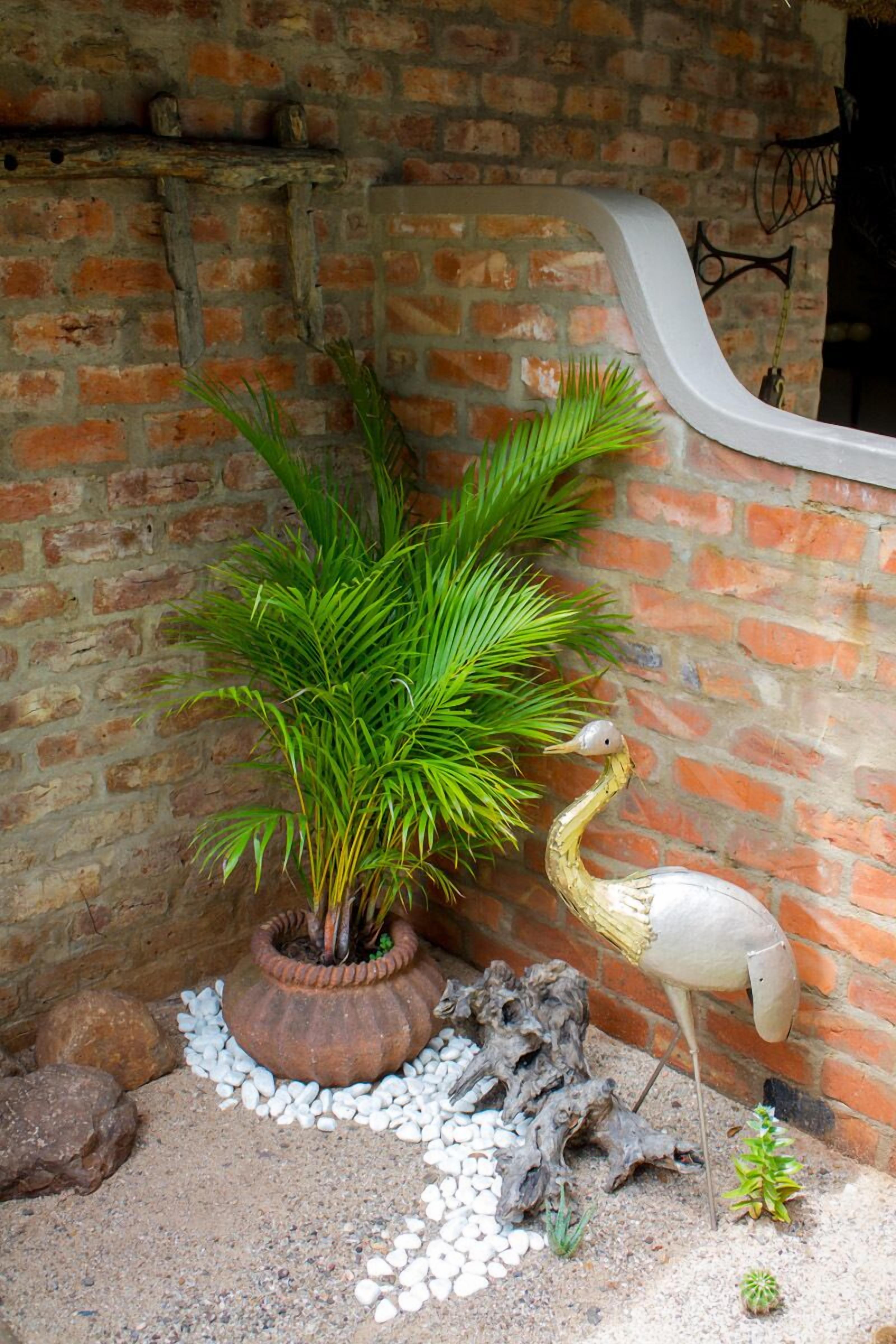 A potted plant with a bird sculpture beside a brick wall.