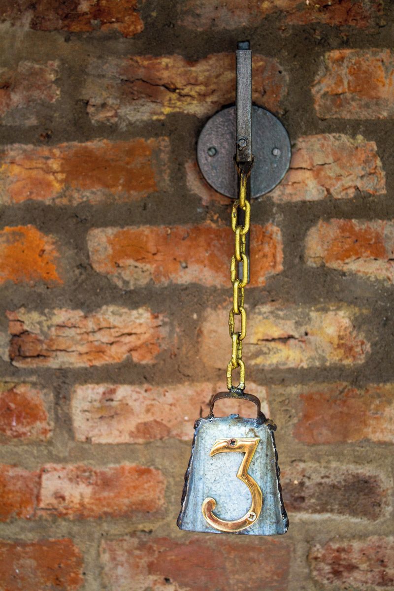 A metal bell with the number 3 hanging on a brick wall.