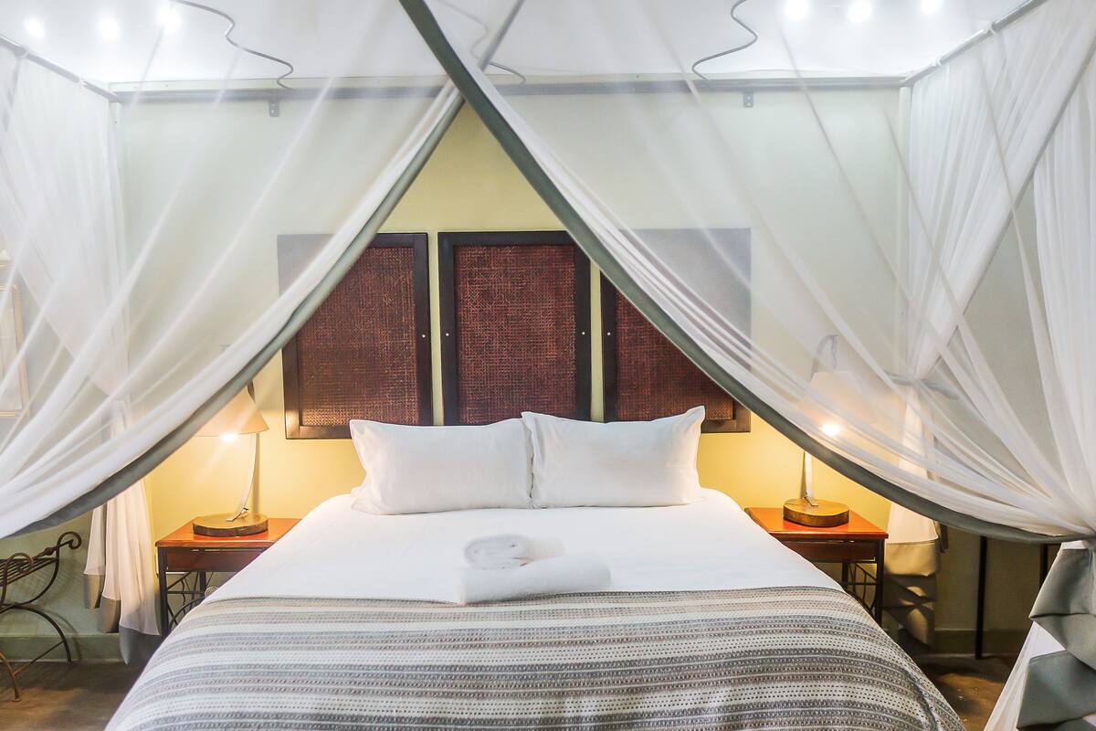 A bed with white bedding, a mosquito net, and two bedside lamps.