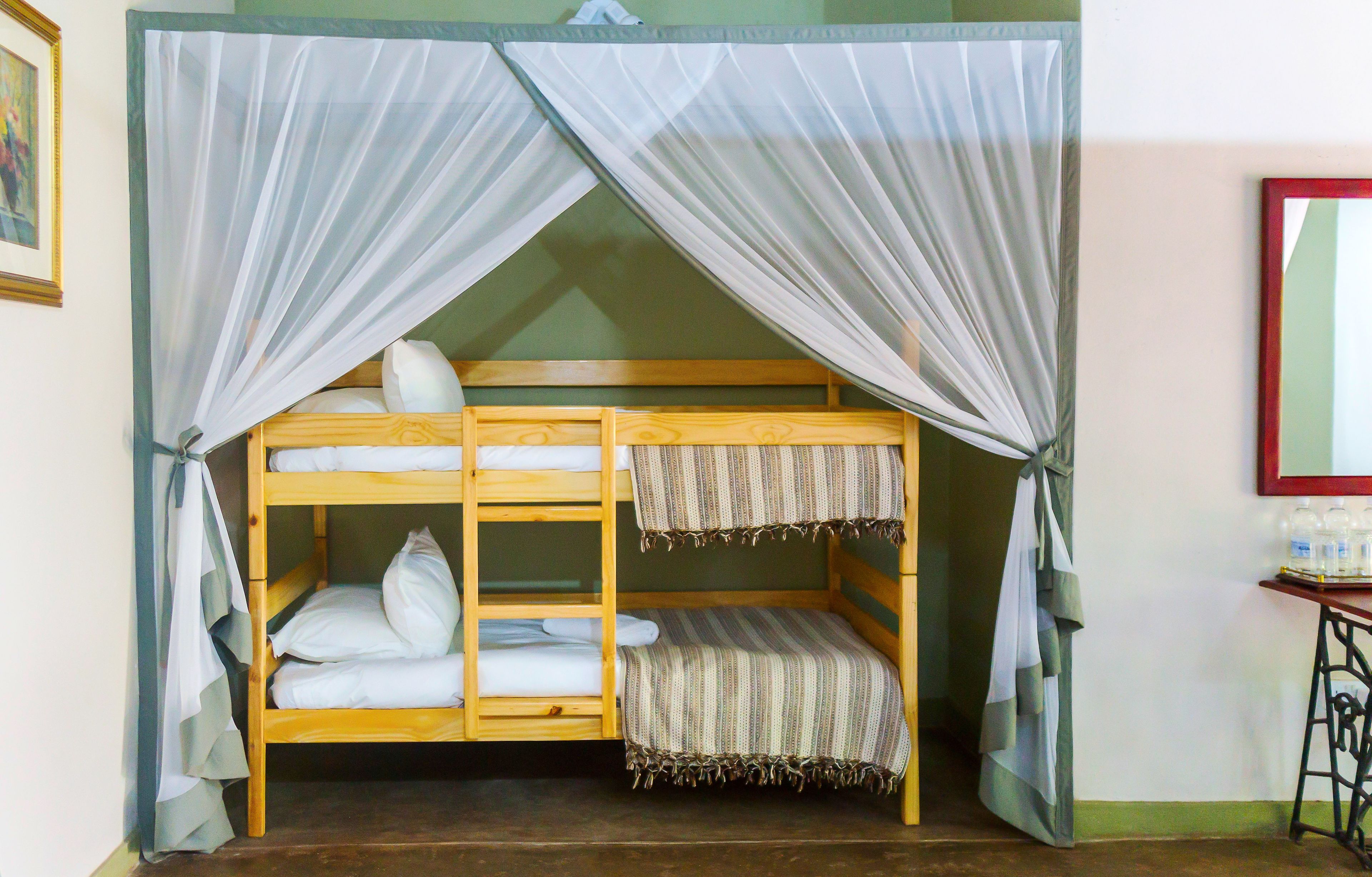 A bunk bed with a mosquito net, a wooden headboard, and a bedside table with a mirror and toiletries.