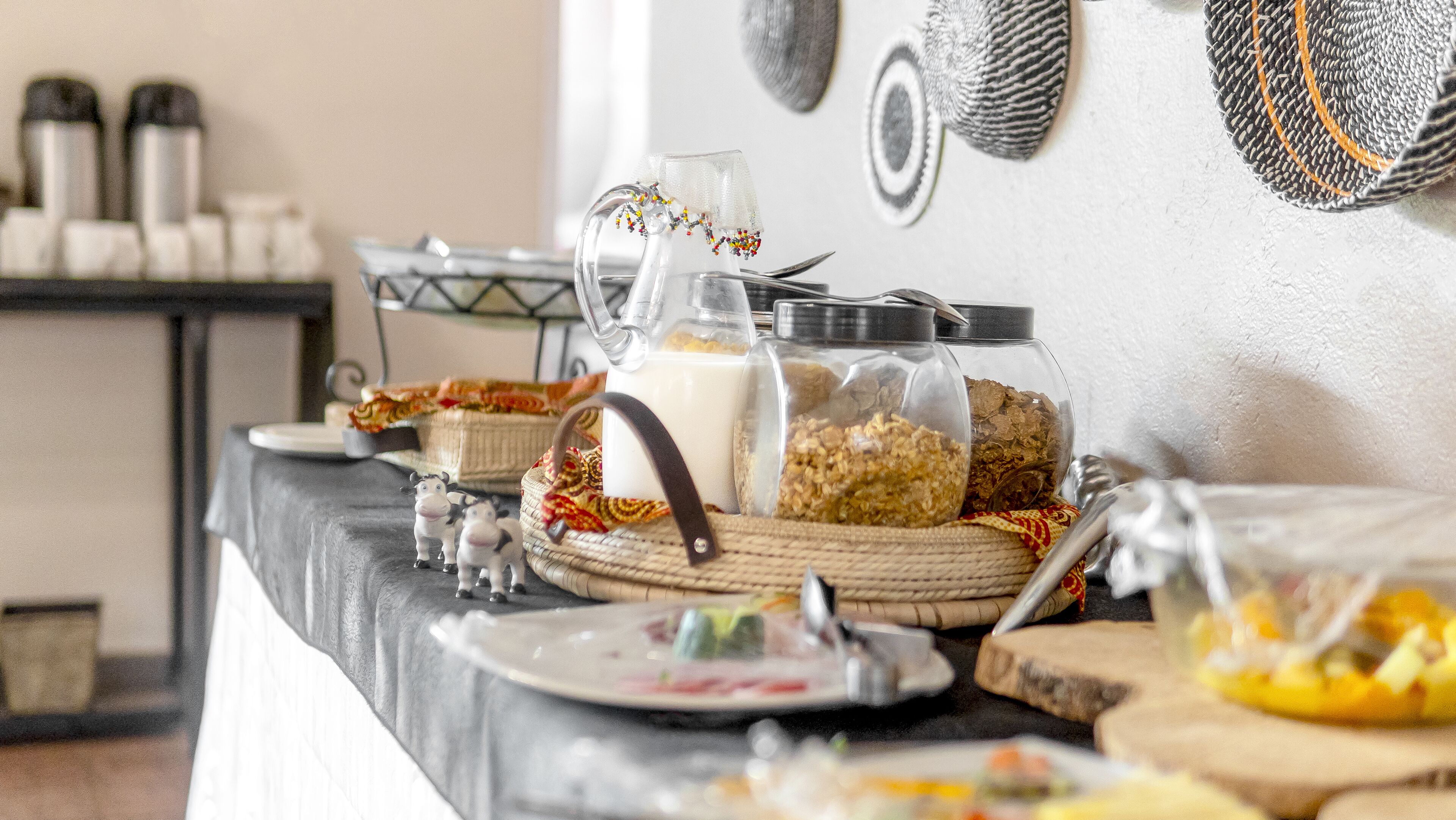 Une table de buffet avec divers plats et récipients, notamment un pichet à lait, des céréales et un panier décoratif.