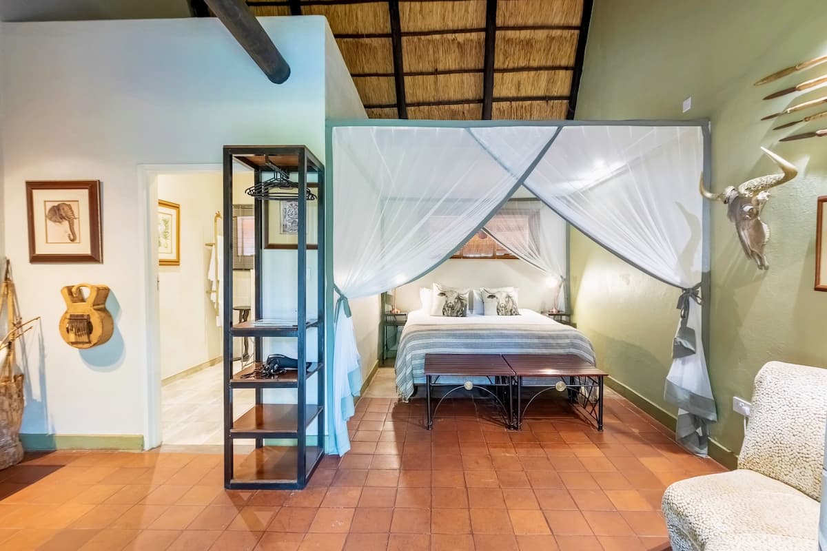 A bedroom with a bed, a canopy, a shelf with items, and wall decorations including a skull and framed pictures.