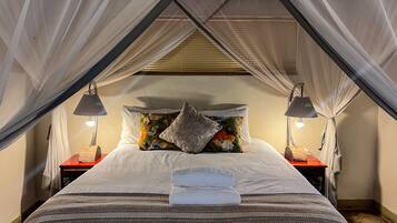 A neatly made bed with a striped blanket, a floral pillow, and a folded towel on top. There are two bedside tables with lamps and a canopy over the bed.