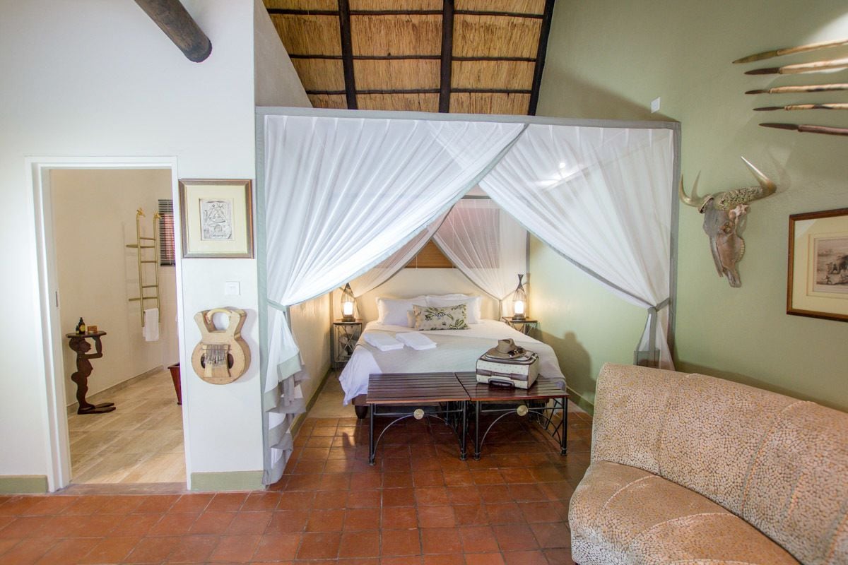 A bedroom with a four-poster bed, a guitar, a suitcase, and a cow skull on the wall.
