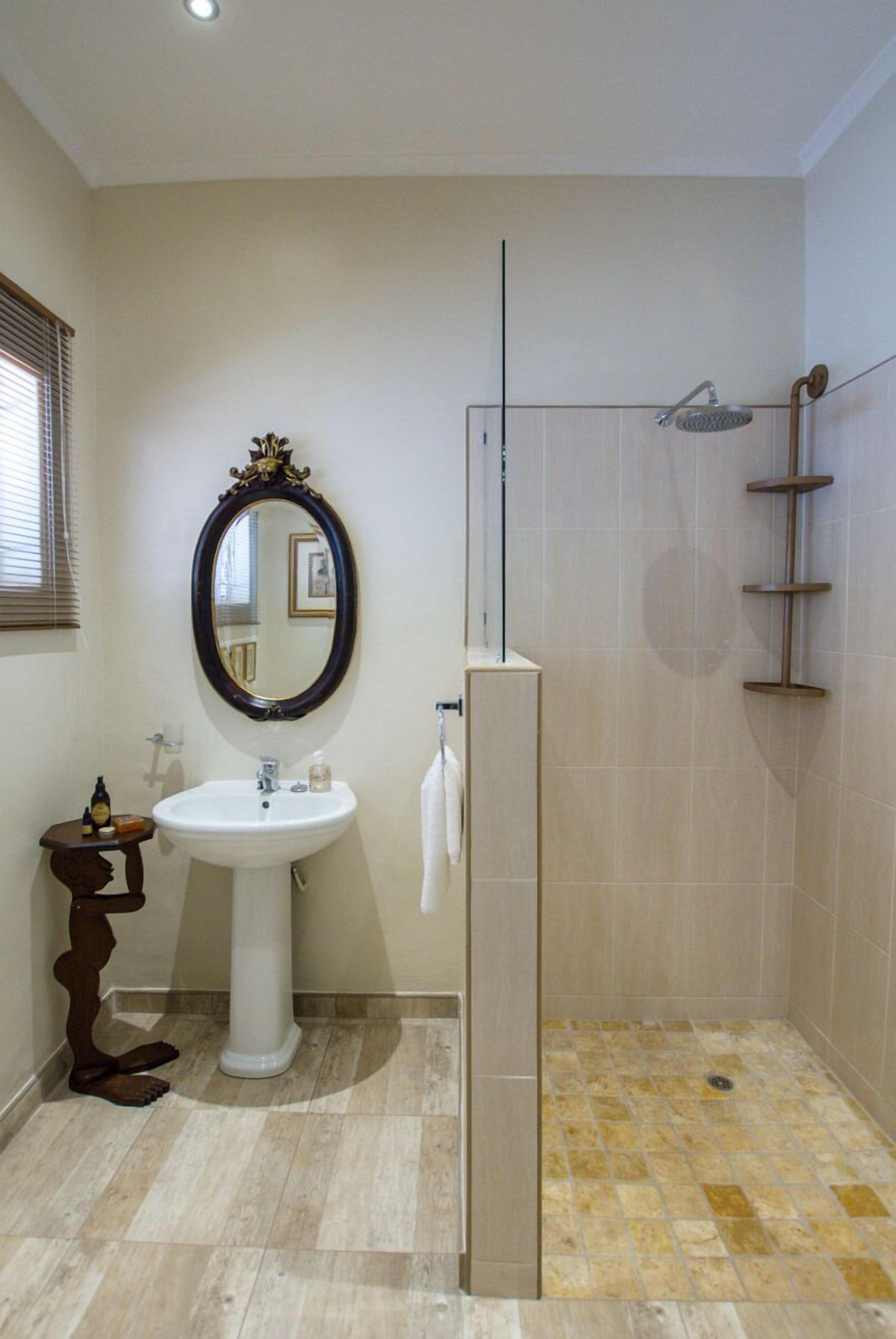 Un baño con lavamanos pedestal, un espejo grande, cabina de ducha y un taburete de madera pequeño.