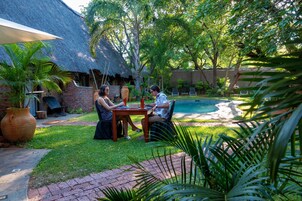 Un patio con una mesa y sillas, rodeado de exuberante follaje y una piscina.