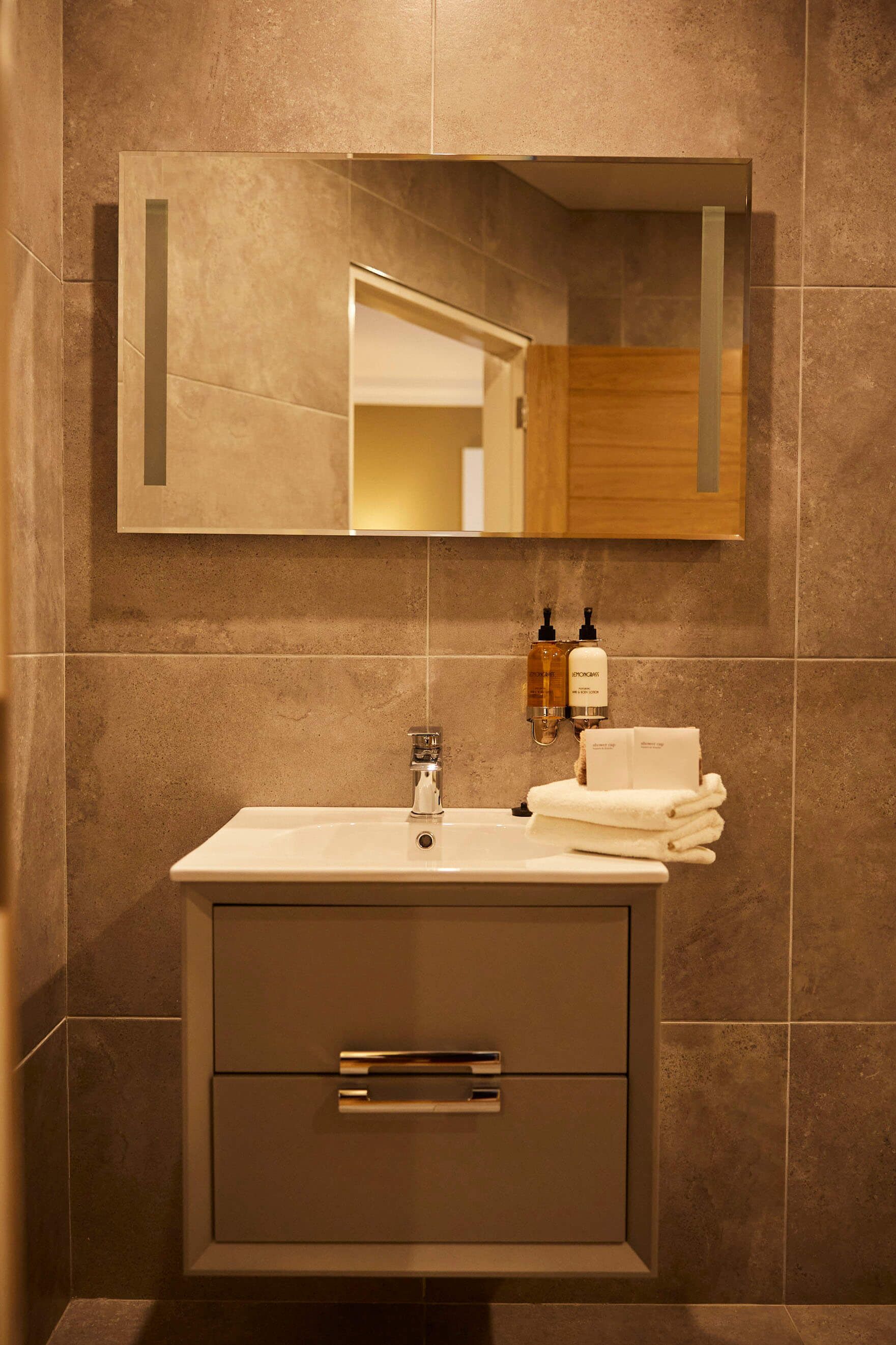 Un baño moderno con un espejo grande, un lavamanos y dos botellas de champú.