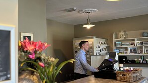 A reception desk with a wooden counter, a teal vase with flowers, a ceiling fan, and a wall-mounted projector.