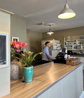 A reception desk with a wooden counter, a teal vase with flowers, a ceiling fan, and a wall-mounted projector.