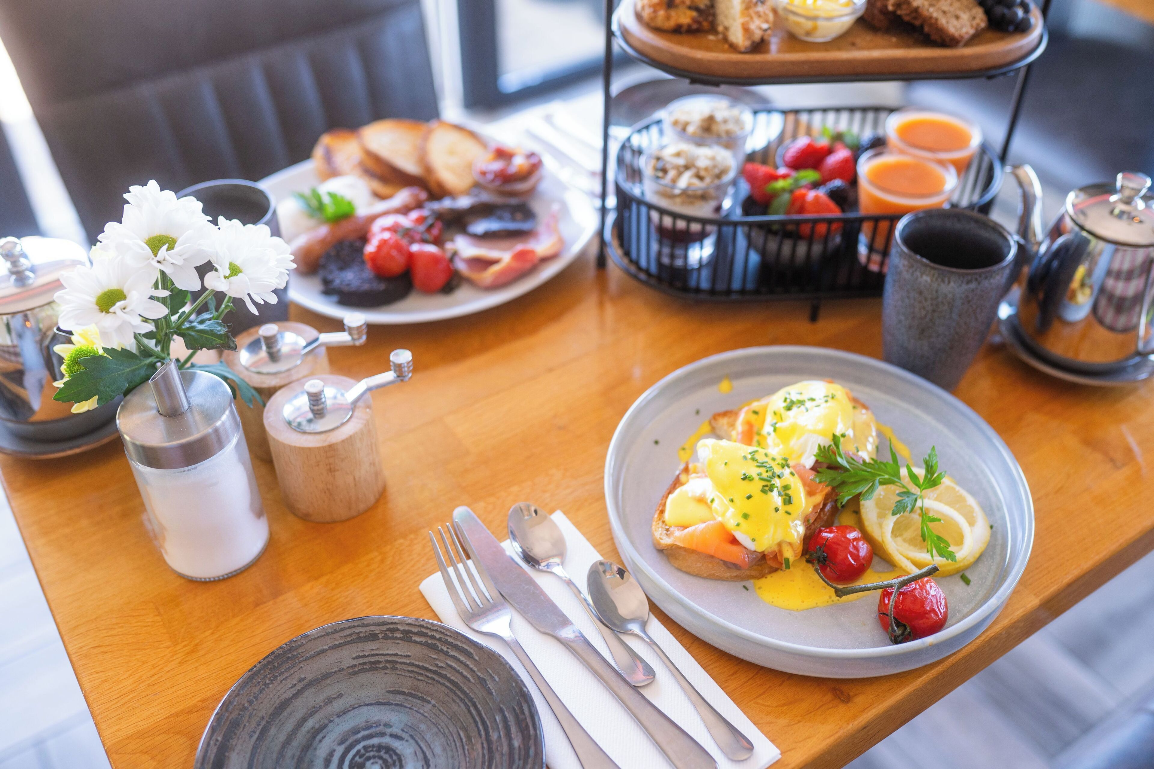 Un desayuno con diversos platos, como huevos, tostadas y frutas, sobre una mesa de madera.