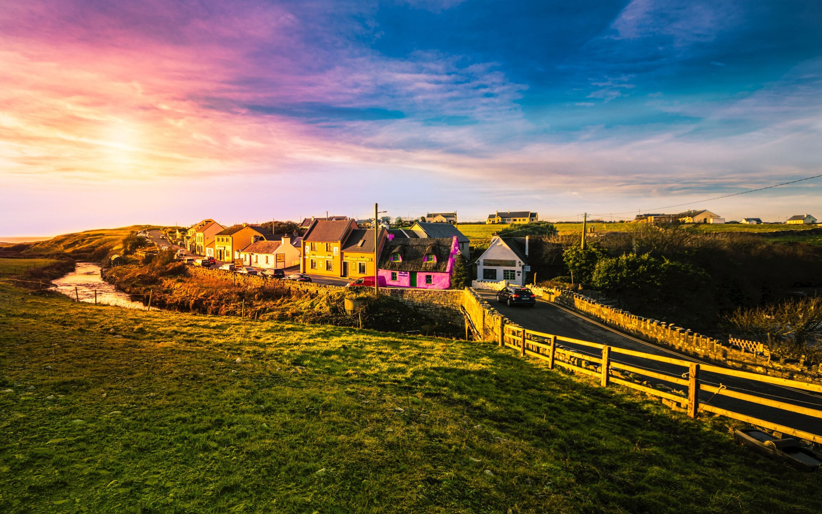 A coastal village with colorful houses, a stone wall, and a road leading through.