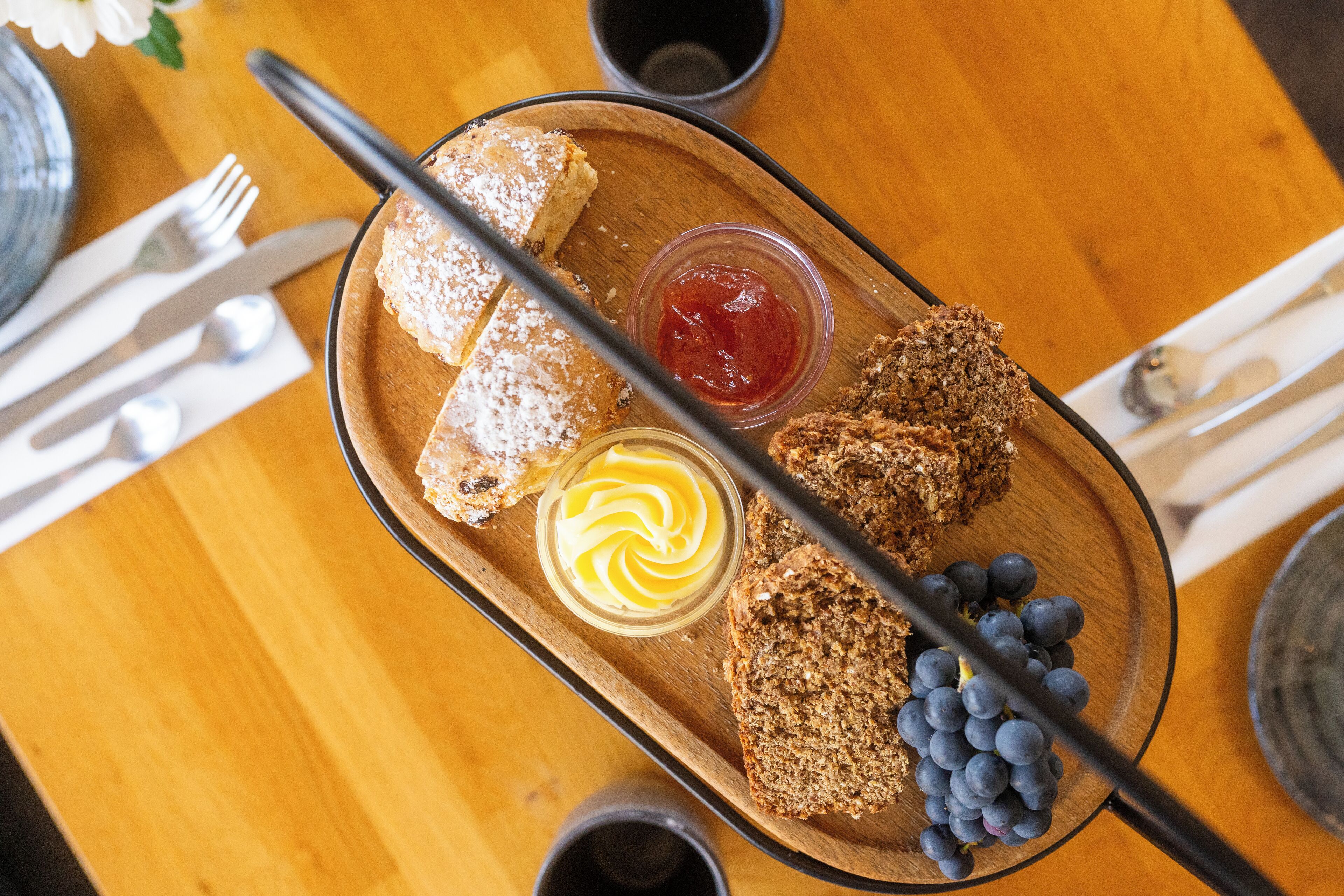 A wooden tray with bread, butter, jam, and blueberries.