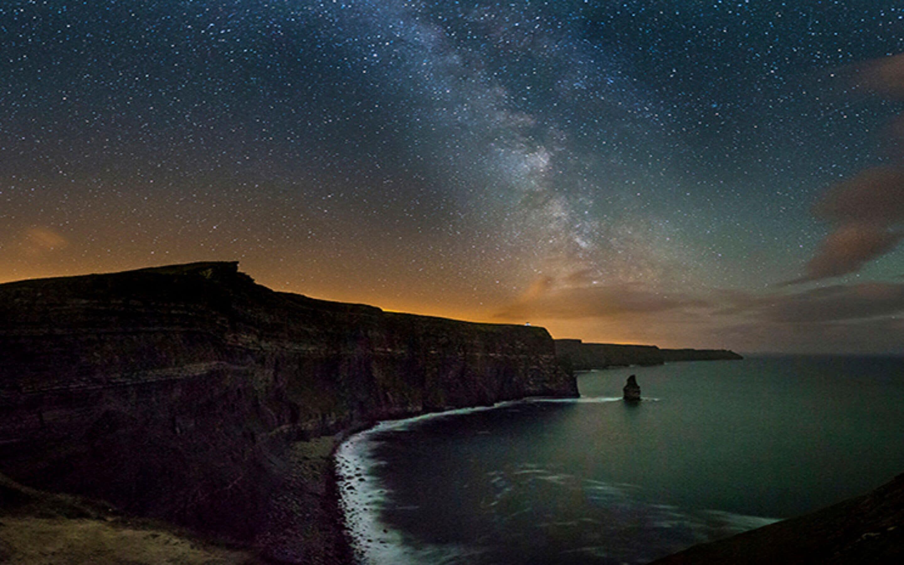 A coastal landscape at night with a starry sky and a visible Milky Way.