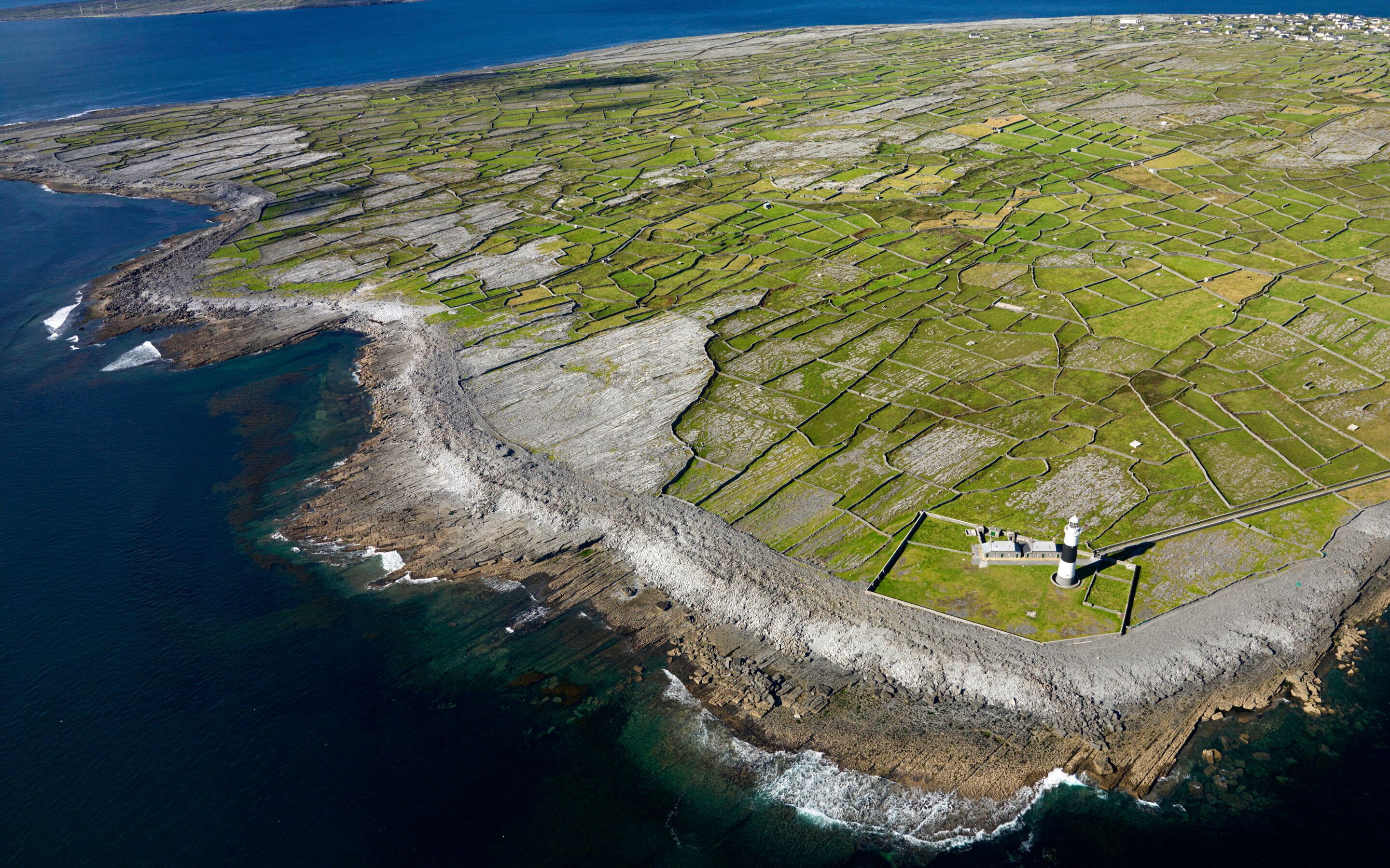 An aerial view of terraced fields and a lighthouse by the coast.