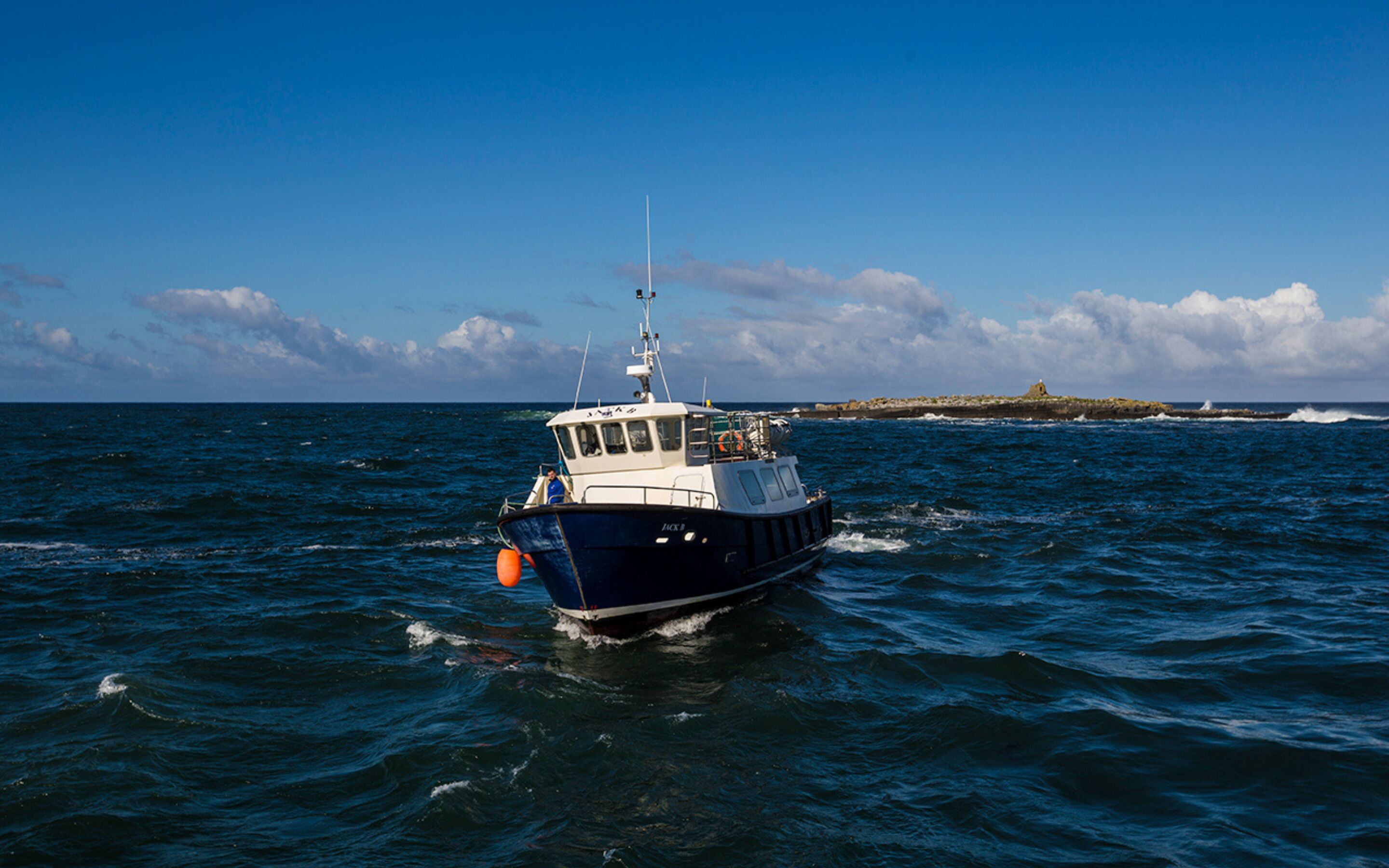 Un bateau sur l’eau, avec une île rocheuse en arrière-plan.