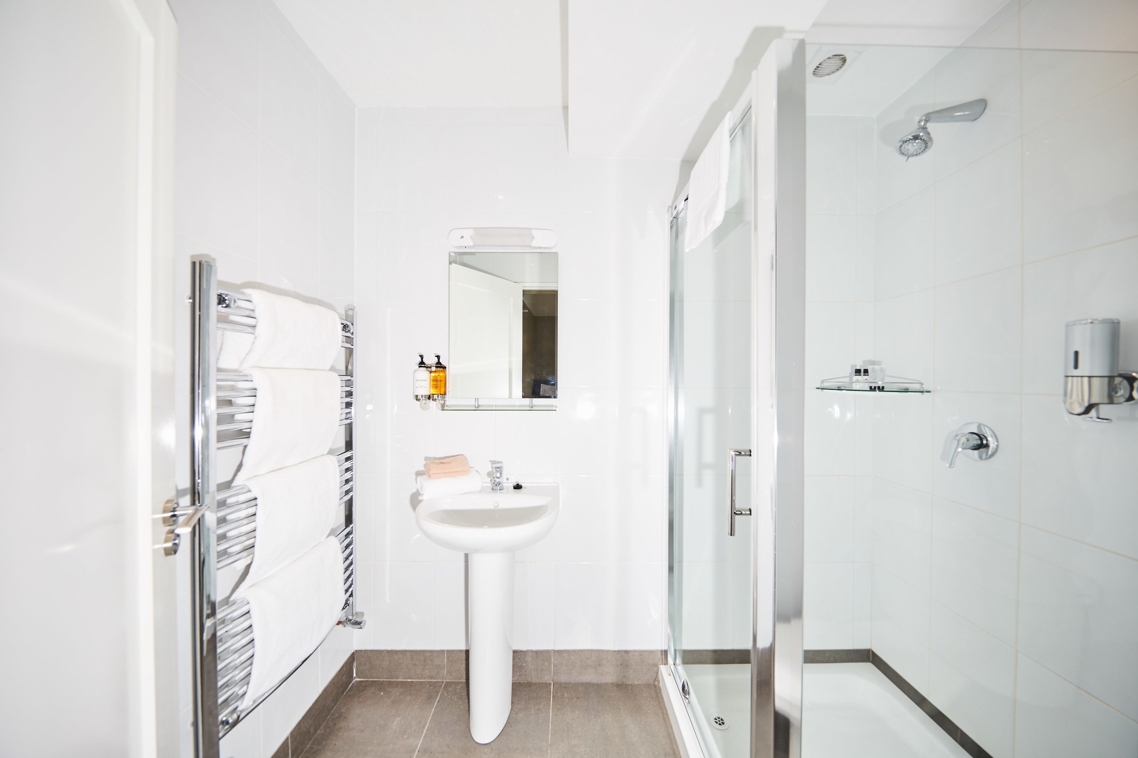Une salle de bain moderne avec une douche à parois de verre, un lavabo sur colonne et un porte-serviettes.