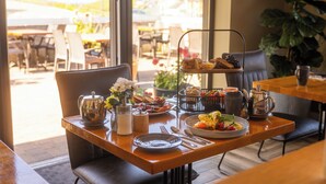 Taula de l'esmorzar amb diversos aliments, com ara pastissos, fruites i begudes, situada en una habitació lluminosa amb vista a l'exterior.