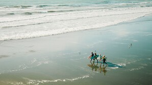 Una platja amb persones caminant i portant taules de surf.