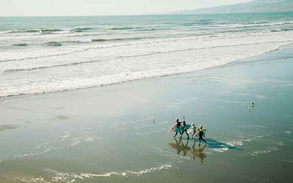 Una playa con gente caminando y llevando tablas de surf.