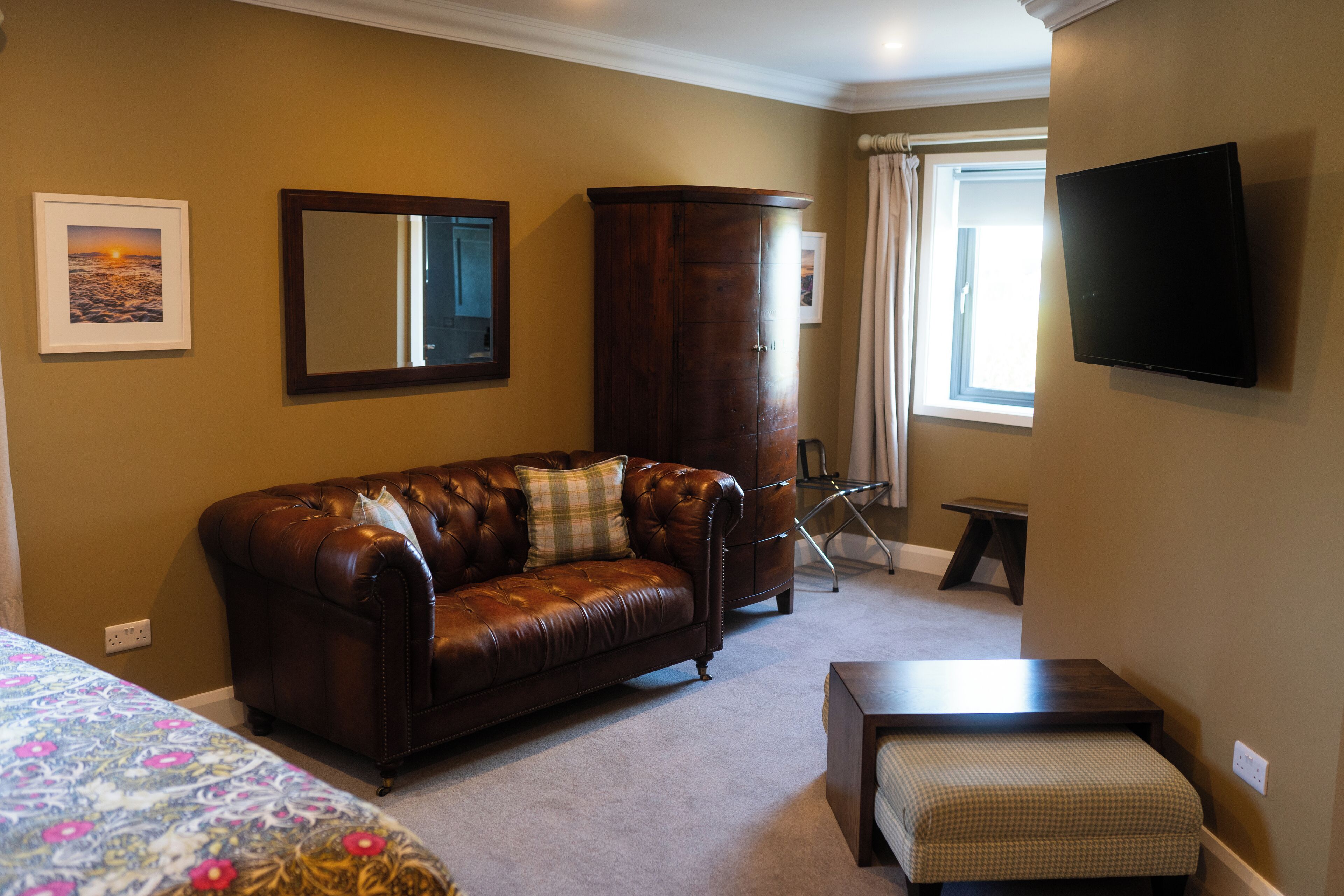 A room with a brown leather sofa, a wooden cabinet, a small table, and a television mounted on the wall.