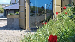 Una construcció petita i oberta amb una porta de vidre, envoltada de grava i flors vermelles.