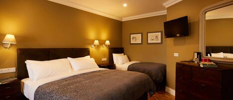 Una habitación de hotel con dos camas, un aparador, un televisor y lámparas fijadas a la pared.