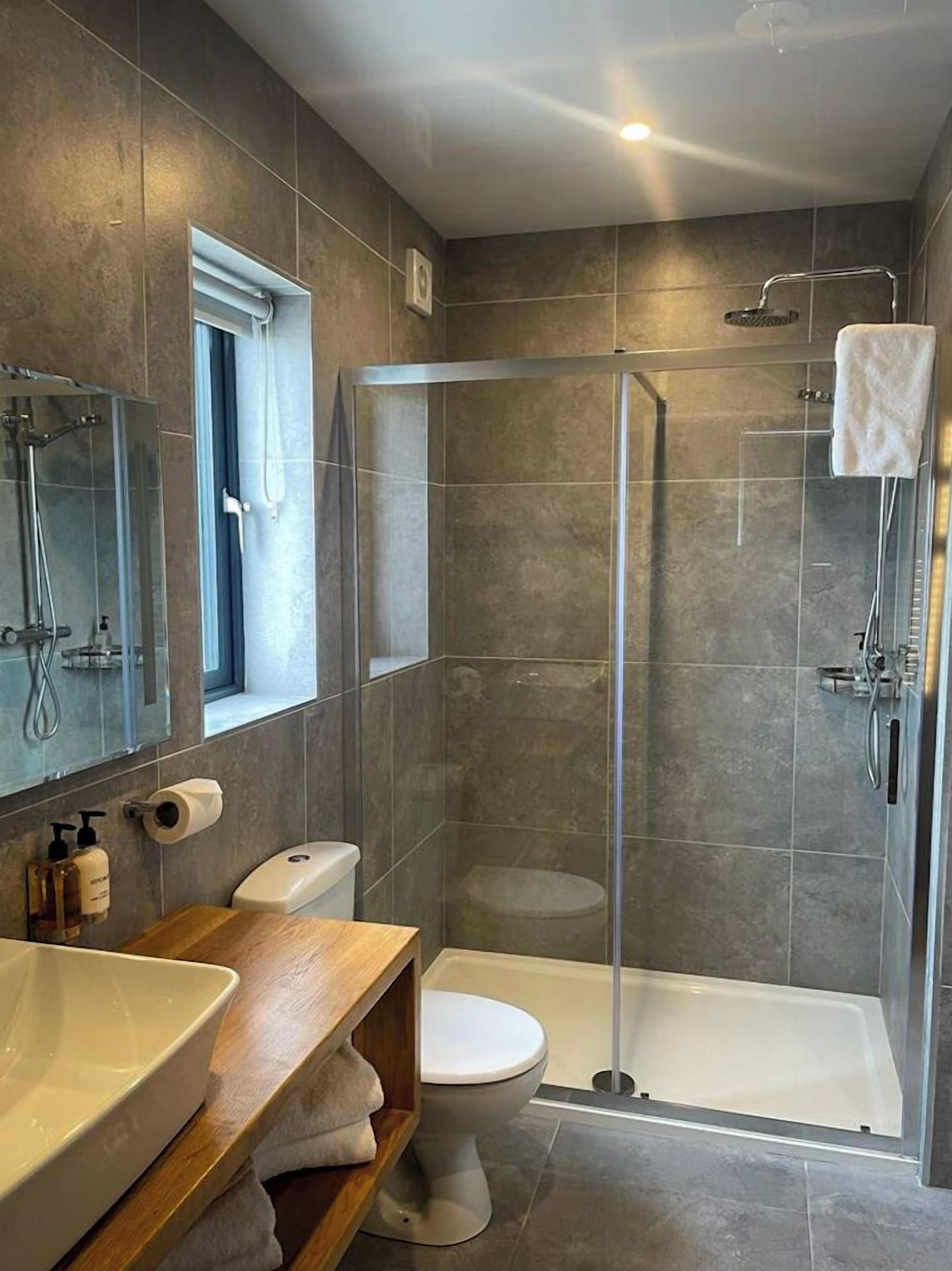 A modern bathroom with a glass-enclosed shower, a wooden vanity, a toilet, and a large mirror.