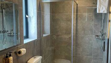 A modern bathroom with a glass-enclosed shower, a wooden vanity, a toilet, and a large mirror.