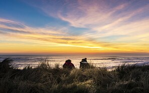 Two people sitting on the beach at sunset, overlooking the ocean.