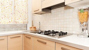 Une cuisine équipée d’une cuisinière à gaz, de carreaux blancs, de meubles en bois et d’une fenêtre agrémentée de rideaux à motifs floraux.