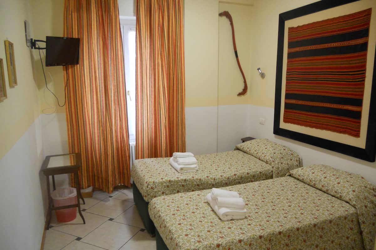 Una habitación con dos camas, un televisor montado en la pared, un radiador y un cuadro.
