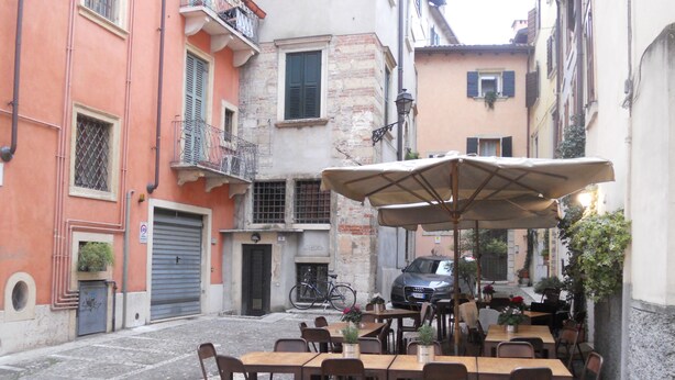 Un café en plein air, avec des tables et des chaises, entouré d’immeubles dotés de balcons et de fenêtres.