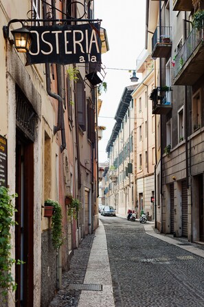 A narrow cobblestone street lined with buildings, a sign reading "OSTERIA a la", and a parked motorcycle. - By Duomo (Verona)