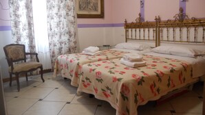 Une chambre avec deux lits, des couvre-lits à motifs floraux, une chaise et un tableau encadré au mur.