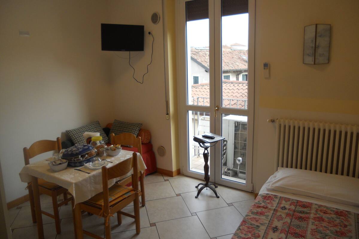 Una habitación pequeña con una mesa de comedor, sillas, una cama, un televisor y una ventana con vistas a edificios.
